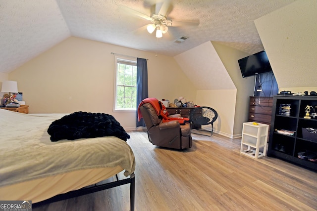 bedroom featuring ceiling fan, a textured ceiling, vaulted ceiling, light wood-type flooring, and visible vents