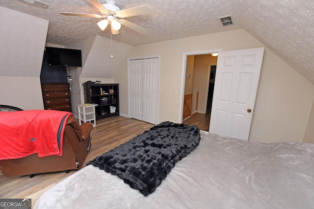 bedroom with a textured ceiling, visible vents, vaulted ceiling, wood finished floors, and a closet