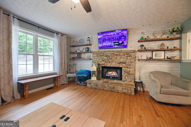 living area with a textured ceiling, ceiling fan, a fireplace, and wood finished floors