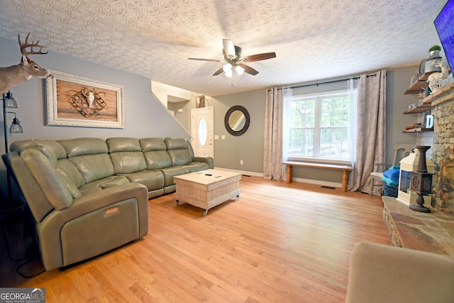 living area featuring light wood finished floors, a textured ceiling, a ceiling fan, baseboards, and visible vents