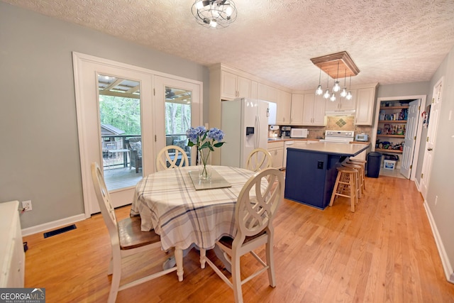 dining room with light wood-type flooring, a textured ceiling, baseboards, and a chandelier