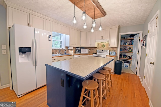 kitchen with a textured ceiling, light wood-type flooring, a sink, under cabinet range hood, and white appliances