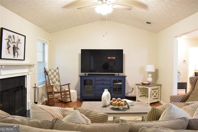 living room featuring a ceiling fan, visible vents, a fireplace, vaulted ceiling, and wood finished floors