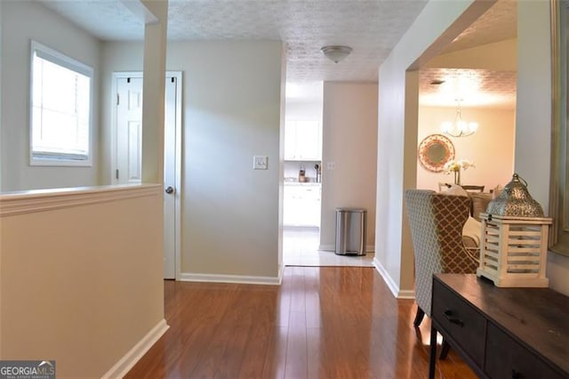 corridor featuring a textured ceiling, baseboards, a notable chandelier, and wood finished floors