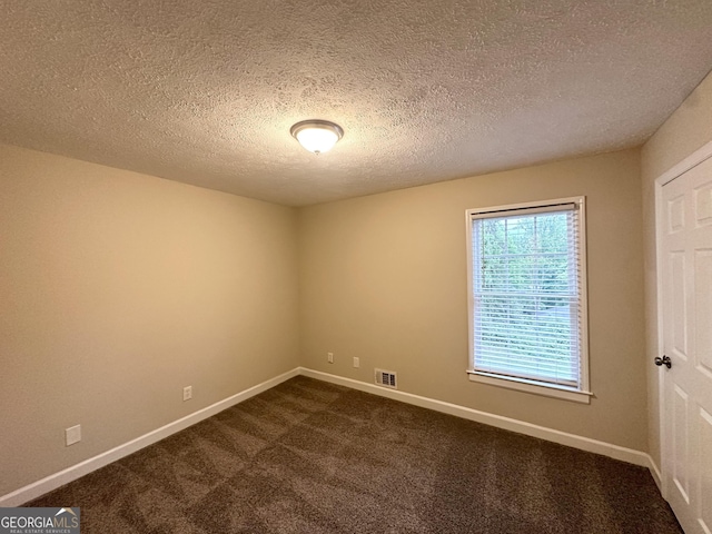 spare room with visible vents, a textured ceiling, baseboards, and dark carpet