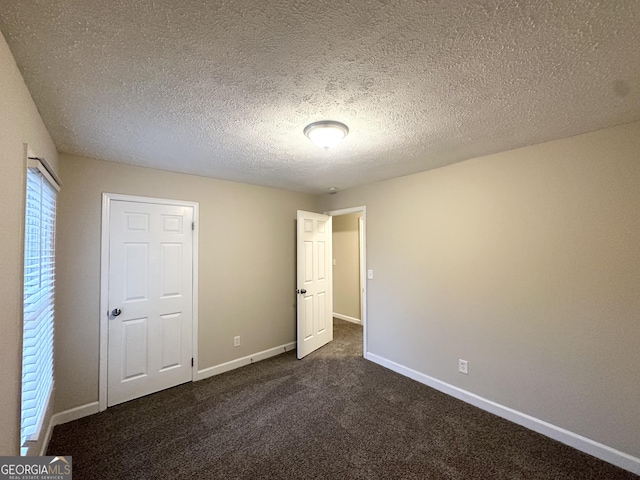 unfurnished bedroom with dark colored carpet, a textured ceiling, and baseboards