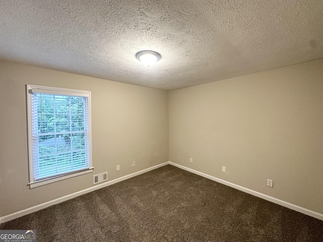 spare room with baseboards, dark colored carpet, a textured ceiling, and visible vents