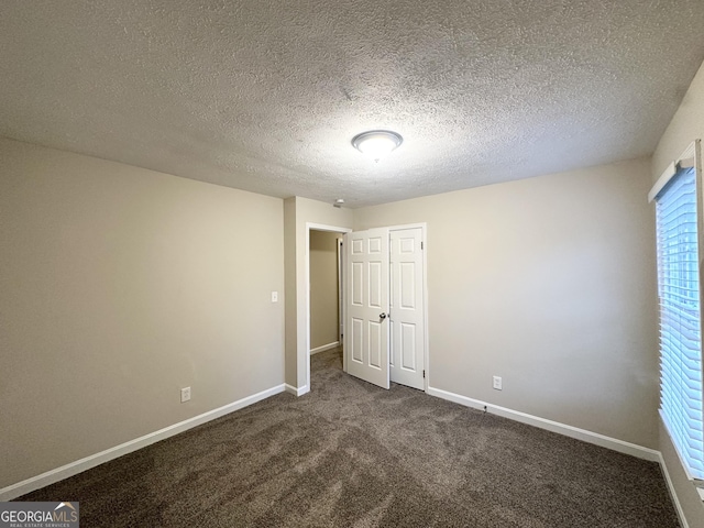 unfurnished bedroom featuring baseboards, dark carpet, and a textured ceiling