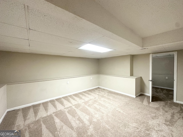 finished below grade area featuring carpet floors, baseboards, and a paneled ceiling
