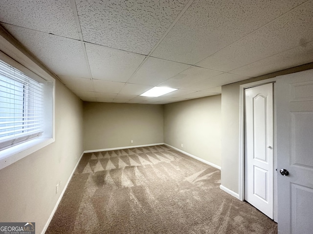 below grade area featuring carpet flooring, baseboards, and a paneled ceiling