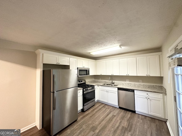 kitchen featuring dark wood-style flooring, appliances with stainless steel finishes, a sink, a textured ceiling, and white cabinetry