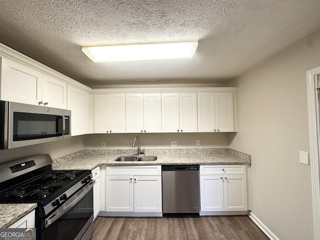 kitchen featuring white cabinets, appliances with stainless steel finishes, a sink, a textured ceiling, and dark wood-type flooring