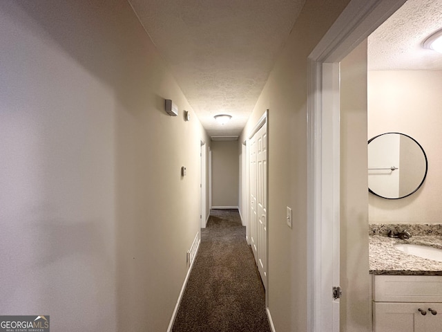 hallway featuring a sink, dark colored carpet, a textured ceiling, and visible vents