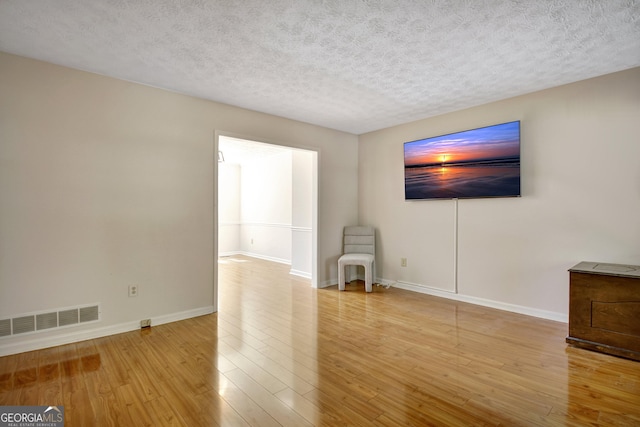 unfurnished living room featuring a textured ceiling, baseboards, wood finished floors, and visible vents