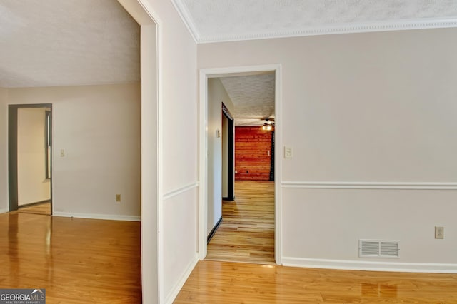 hall featuring visible vents, ornamental molding, baseboards, a textured ceiling, and light wood-style flooring
