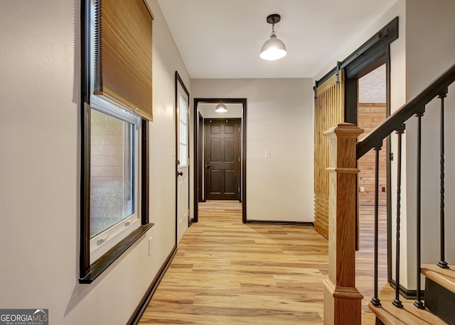 hallway featuring light wood-style floors, a barn door, baseboards, and stairs