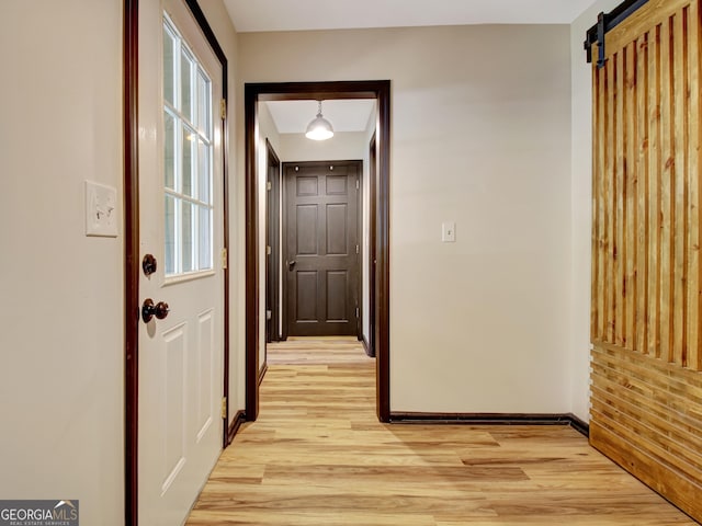 hallway featuring baseboards, a barn door, and light wood-style flooring