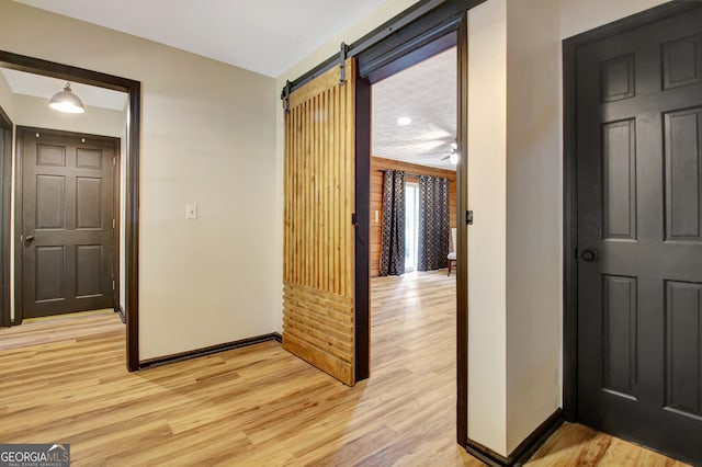 hall with baseboards, a barn door, and light wood-type flooring