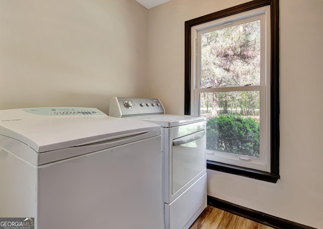 clothes washing area with laundry area, washing machine and dryer, and light wood-style flooring