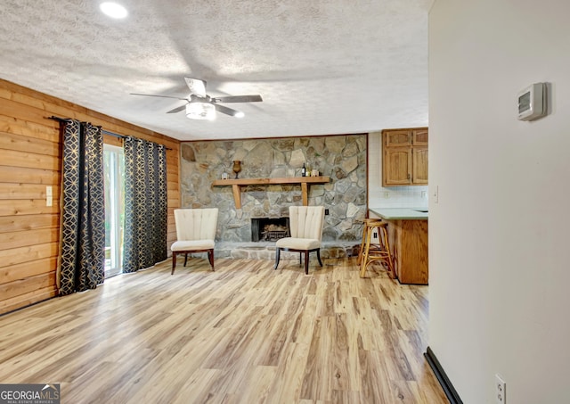 sitting room with light wood-type flooring, wood walls, a textured ceiling, and ceiling fan