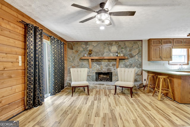 living area featuring light wood-style flooring, a textured ceiling, ceiling fan, and a fireplace