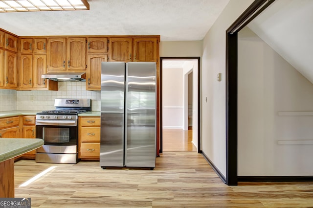 kitchen featuring appliances with stainless steel finishes, decorative backsplash, under cabinet range hood, and light wood finished floors