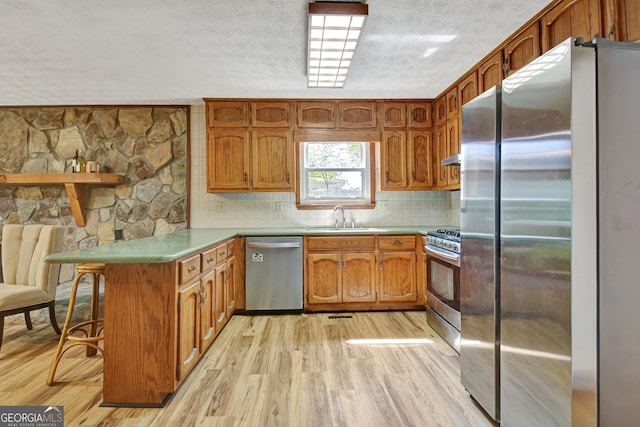 kitchen featuring appliances with stainless steel finishes, a sink, a textured ceiling, light wood-style flooring, and a peninsula