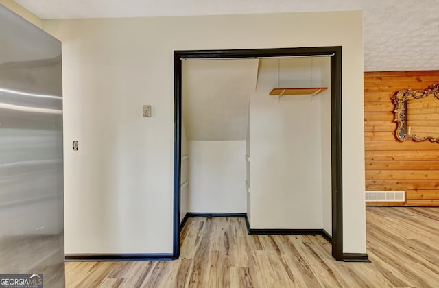hallway with visible vents, light wood finished floors, baseboards, and wooden walls