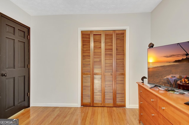 bedroom featuring baseboards, a closet, light wood finished floors, and a textured ceiling