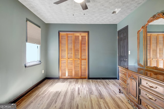 unfurnished bedroom with ceiling fan, a textured ceiling, baseboards, a closet, and light wood finished floors