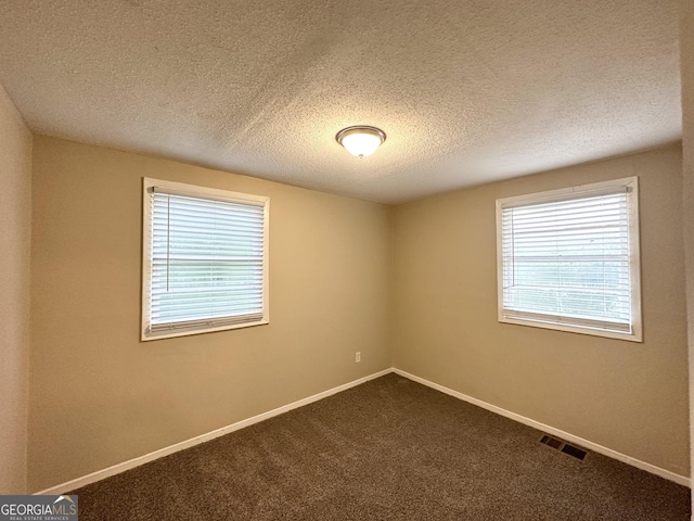 spare room featuring baseboards, dark carpet, a textured ceiling, and visible vents