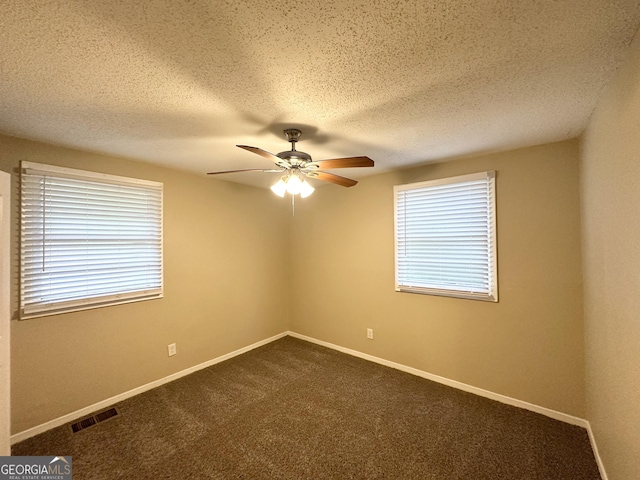 spare room with a ceiling fan, visible vents, a healthy amount of sunlight, and dark carpet