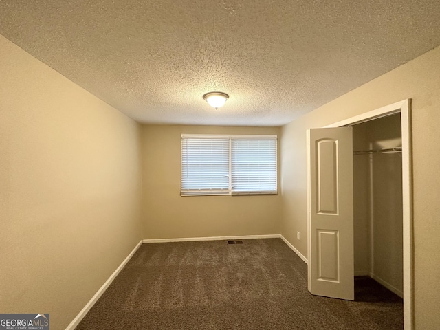unfurnished bedroom with a textured ceiling, visible vents, baseboards, a closet, and dark colored carpet