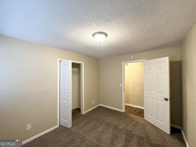 unfurnished bedroom featuring a closet, baseboards, a textured ceiling, and dark colored carpet