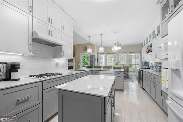 kitchen featuring white gas cooktop, a center island, a peninsula, tasteful backsplash, and gray cabinetry