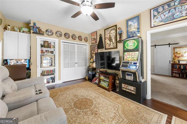 living room with a ceiling fan, a barn door, french doors, and wood finished floors