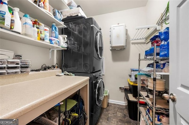 washroom featuring baseboards, laundry area, stone finish flooring, and stacked washer / dryer