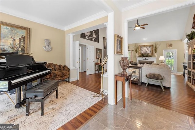living area with ceiling fan, crown molding, wood finished floors, baseboards, and ornate columns