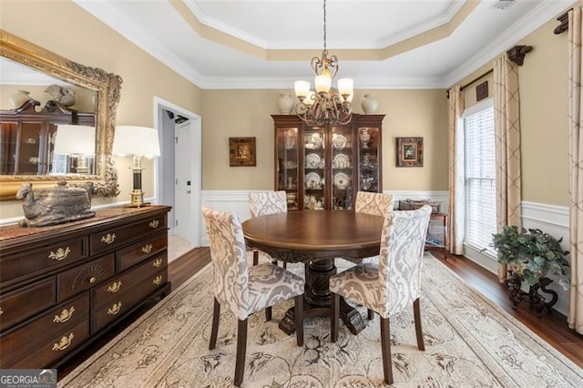 dining area with a chandelier, light wood-style flooring, a raised ceiling, and a wainscoted wall
