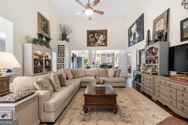 living area with a ceiling fan, wood finished floors, and a towering ceiling