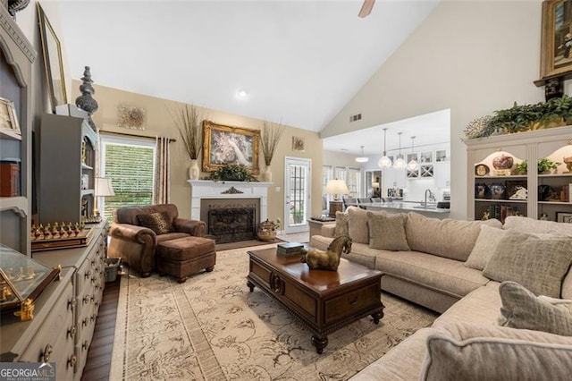 living area featuring visible vents, a ceiling fan, wood finished floors, high vaulted ceiling, and a fireplace with flush hearth
