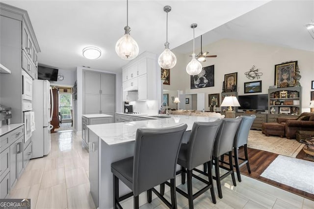 kitchen with a sink, white appliances, gray cabinets, a peninsula, and open floor plan