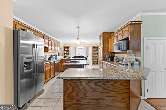 kitchen featuring brown cabinetry, hanging light fixtures, light tile patterned floors, a peninsula, and stainless steel appliances