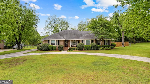 ranch-style home featuring brick siding, curved driveway, fence, and a front yard