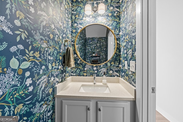 bathroom with vanity, baseboards, wallpapered walls, and wood finished floors