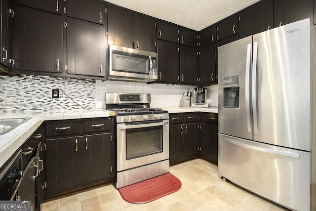 1239 Sharonton Dr, Stone Mountain, GA 30083 - kitchen featuring stainless steel appliances, tile counters, backsplash, and dark cabinetry