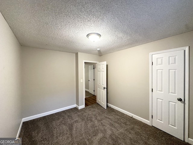 unfurnished bedroom with dark colored carpet, a textured ceiling, and baseboards