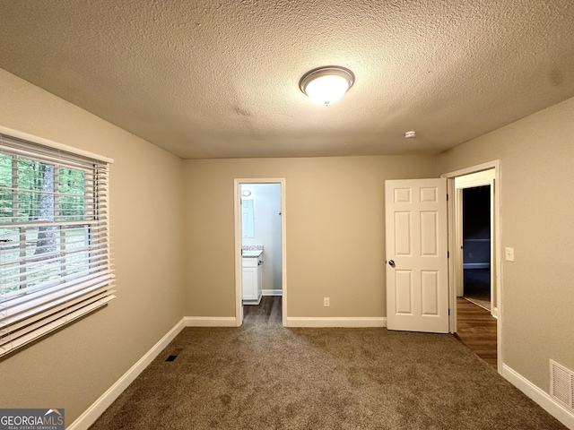 unfurnished bedroom featuring dark colored carpet, a textured ceiling, and baseboards