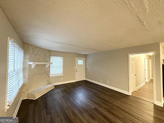 unfurnished living room featuring dark wood-style flooring, a textured ceiling, baseboards, and a fireplace