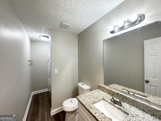 half bath featuring a textured ceiling, wood finished floors, vanity, baseboards, and toilet